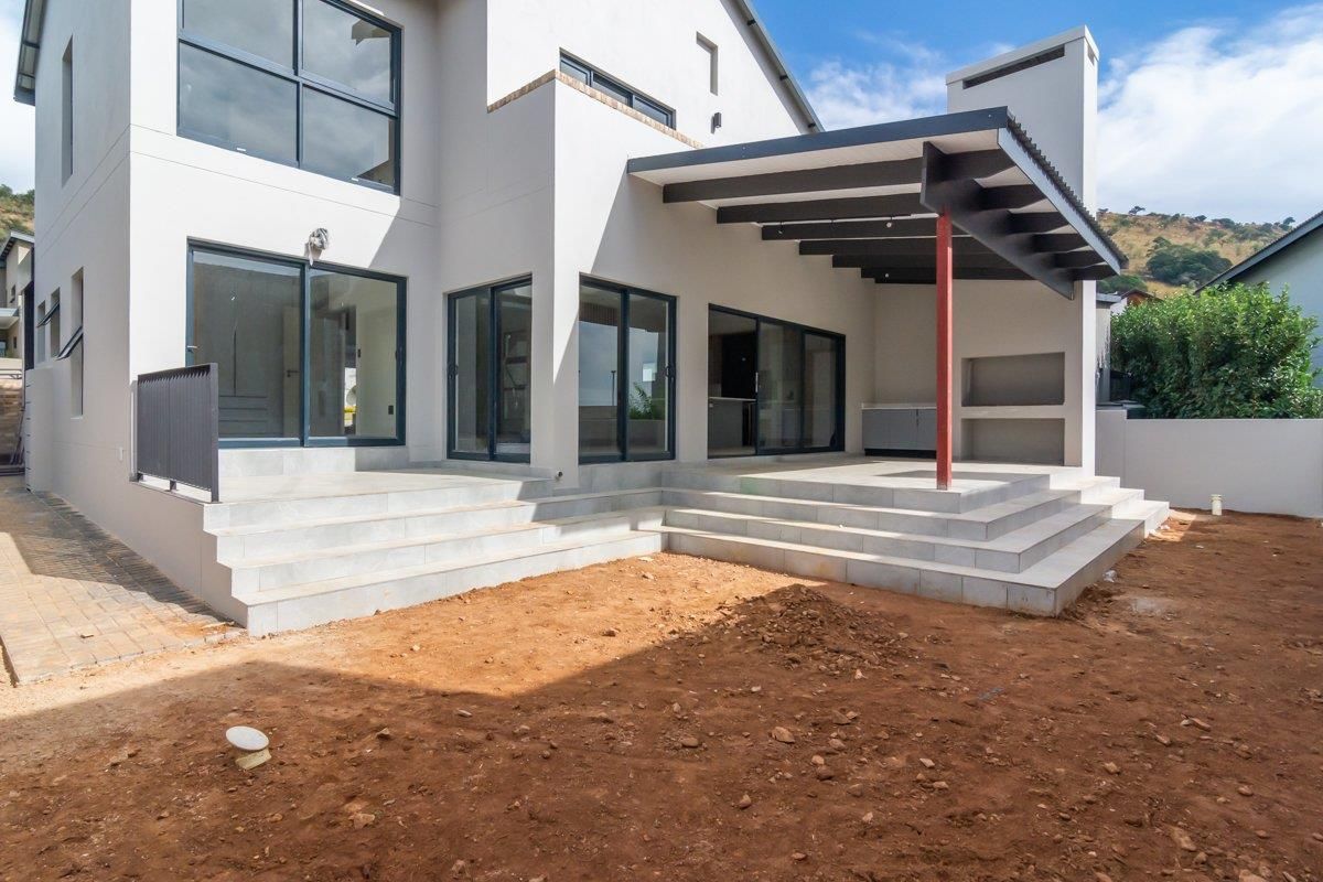 Rear view of a modern double-story house featuring a covered patio with a built-in braai area and tiled steps leading to an unlandscaped garden.