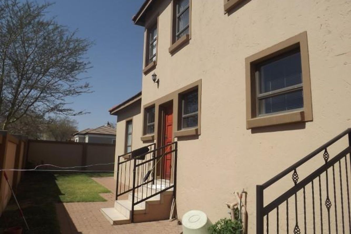 Rear exterior view of the townhouse featuring a paved patio area, external staircase with wrought iron railings, and a surrounding boundary wall.