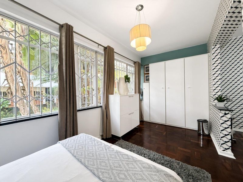 A well-maintained bedroom featuring classic parquet flooring, ample built-in cupboard storage, and large windows fitted with security bars for added peace of mind.