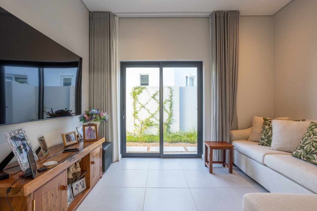 A bright living room featuring large sliding glass doors that open to a private garden area, complemented by neutral tiled flooring and modern finishes.