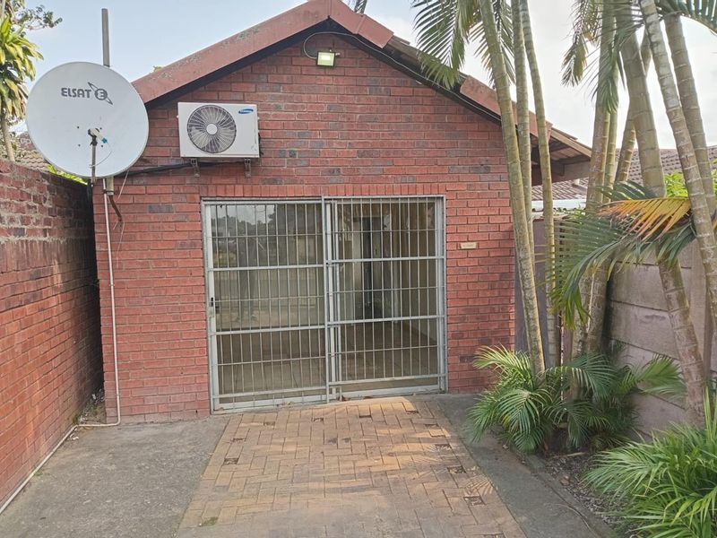 Exterior view of a face brick building featuring a sliding security gate, external air conditioning unit, and a paved walkway.