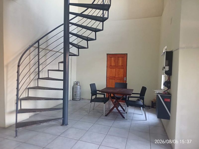 Open plan living area featuring a metal spiral staircase, tiled flooring, and a wall-mounted electrical distribution board.