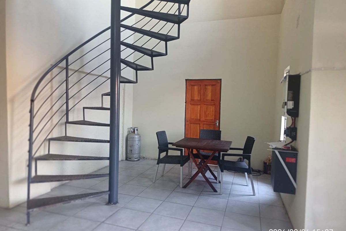 Open plan living area featuring a metal spiral staircase, tiled flooring, and a wall-mounted electrical distribution board.