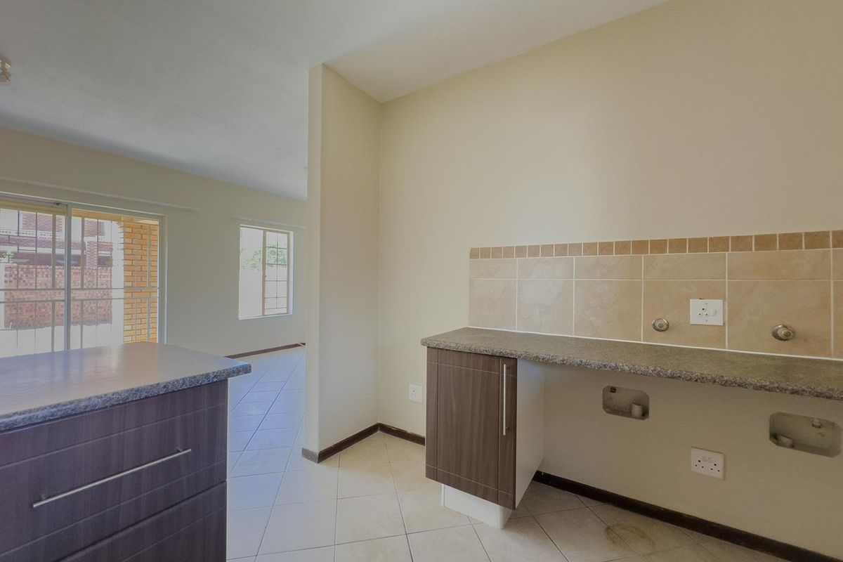 A functional kitchen area featuring dark wood-finish cabinetry, granite-look countertops, and tiled splashbacks, with an open-plan layout leading to the living space.