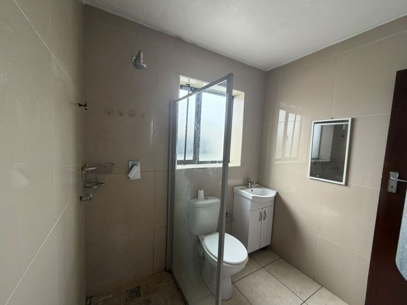 A functional bathroom featuring a glass-enclosed shower, vanity cabinet with basin, and neutral wall tiling throughout.