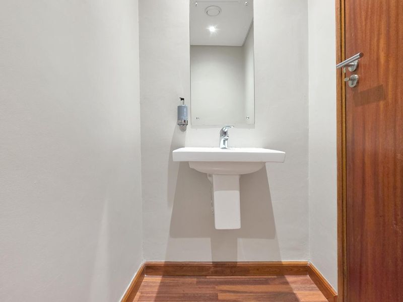 A clean and minimalist guest bathroom featuring a white pedestal basin, chrome tapware, and a wall-mounted mirror with timber flooring and door trim.
