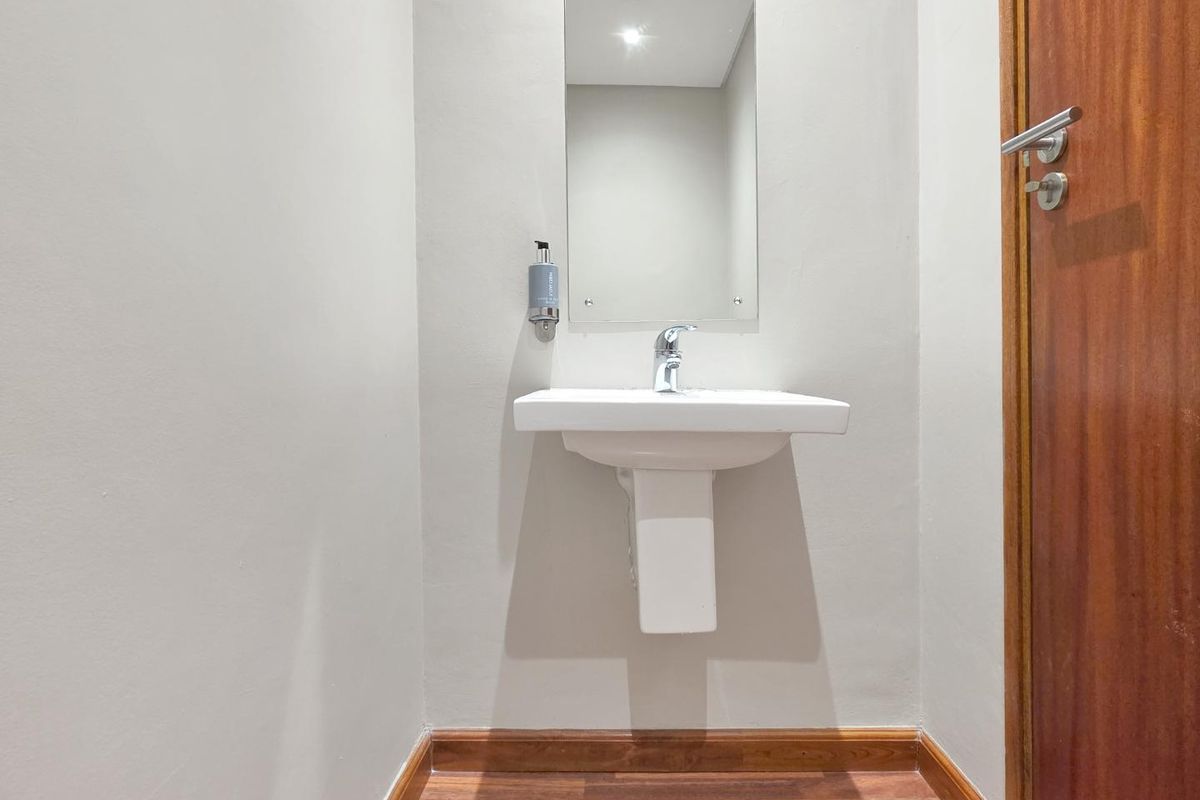 A clean and minimalist guest bathroom featuring a white pedestal basin, chrome tapware, and a wall-mounted mirror with timber flooring and door trim.