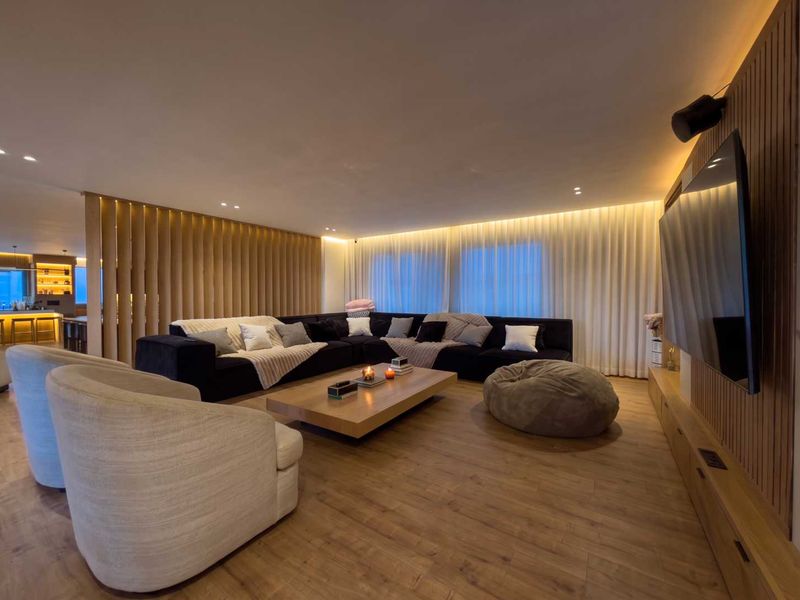 Modern living room featuring warm timber slat wall paneling, recessed cove lighting, and high-quality laminate wood flooring with integrated media cabinetry.