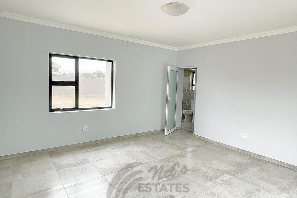 A bright, empty bedroom featuring neutral tiled flooring, large window, and an en-suite bathroom access.