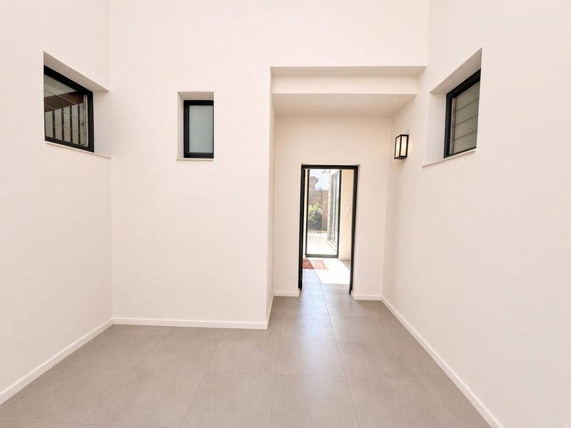 A bright and modern entrance hall featuring neutral tiled flooring, clean white walls, and black-framed windows, leading through to an outdoor area.