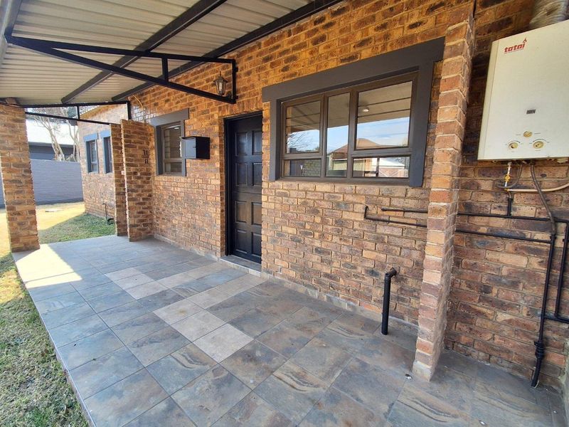 A covered patio area featuring face brick walls, tiled flooring, and an external gas geyser unit.