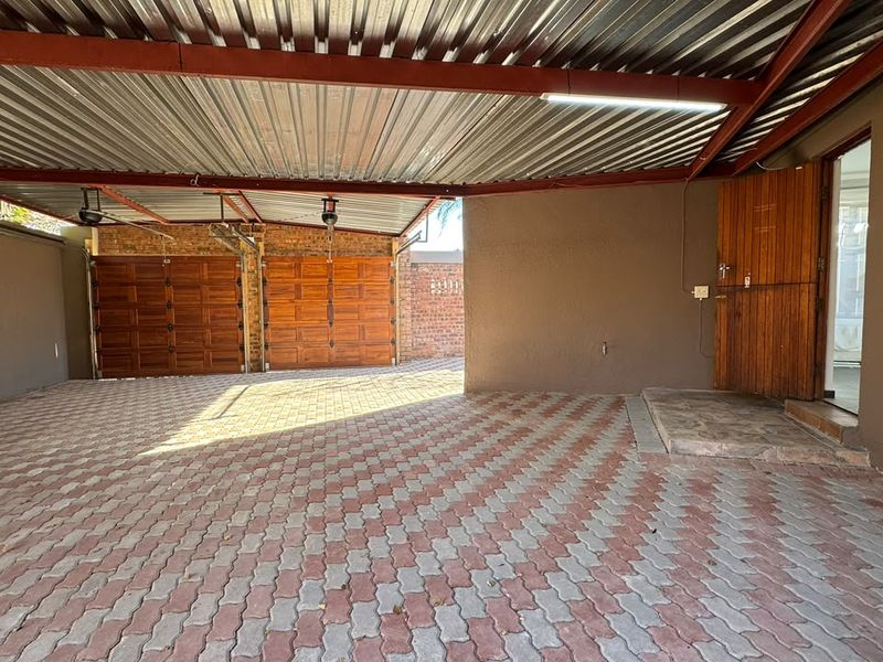 A spacious covered parking area featuring paved flooring, dual wooden garage doors, and direct access to the main house entrance.