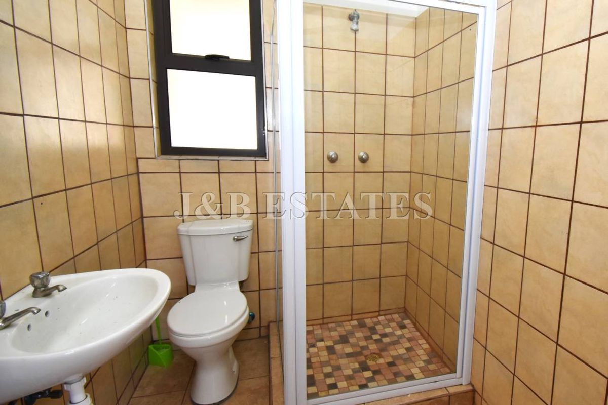 A functional bathroom featuring a shower enclosure, pedestal basin, and toilet with neutral wall and floor tiling.