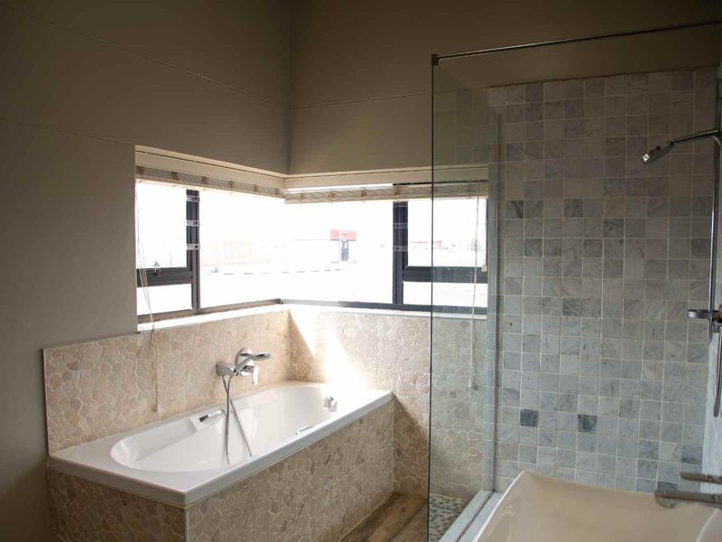 Modern bathroom featuring a built-in bathtub, a glass-enclosed shower with tiled walls, and a corner window providing natural light.