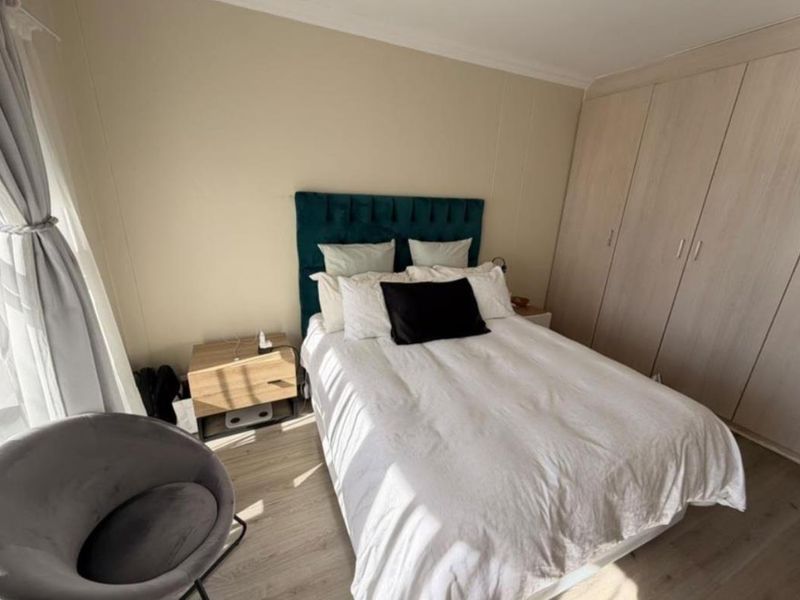 A well-maintained bedroom featuring light-toned laminate flooring, neutral wall finishes, and ample built-in cupboard storage.