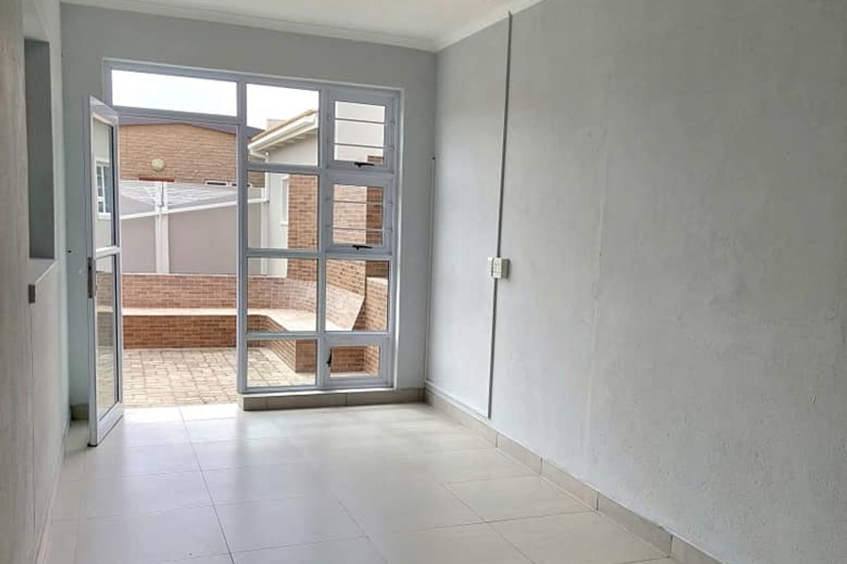 A bright, empty living space featuring neutral floor tiles, a simple ceiling light fixture, and a glass door providing direct access to an outdoor patio.