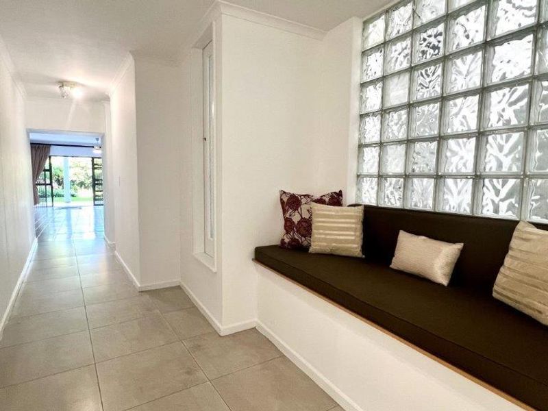A bright hallway featuring a unique glass block feature wall and a built-in bench seat, leading through to an open-plan living area.