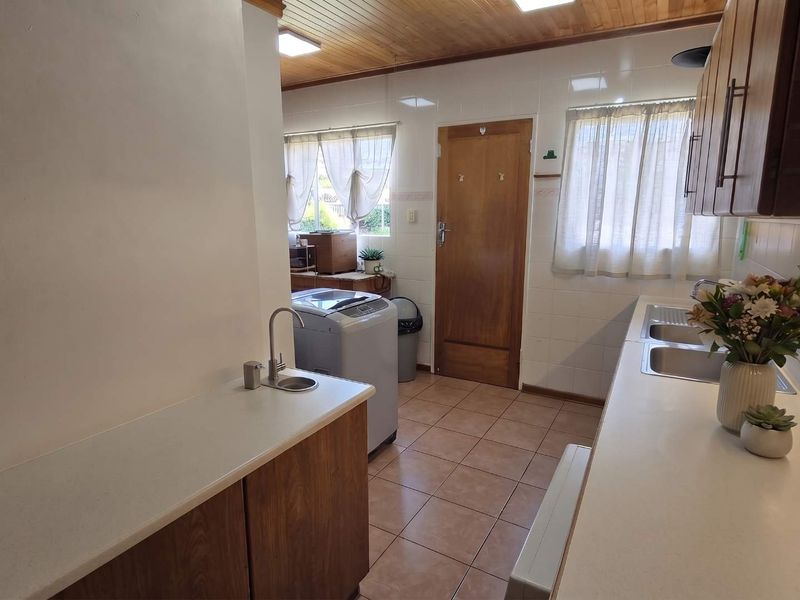 Functional scullery area featuring timber cabinetry, double stainless steel sink, secondary prep sink, tiled splashbacks, and tiled flooring.