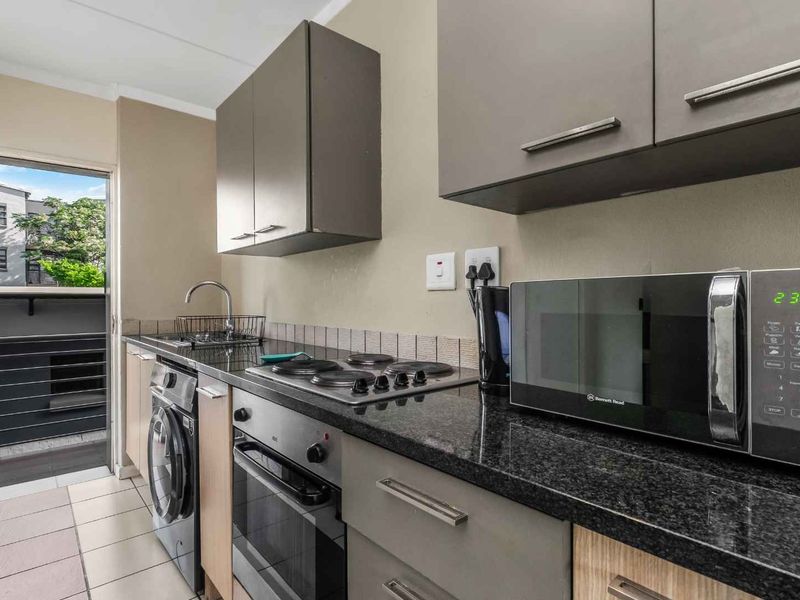 Compact modern kitchen featuring granite countertops, built-in oven and hob, integrated washing machine, and direct access to a private balcony.