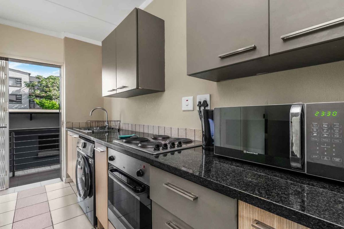 Compact modern kitchen featuring granite countertops, built-in oven and hob, integrated washing machine, and direct access to a private balcony.