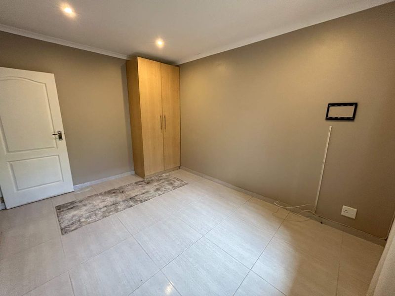 A clean, empty bedroom featuring neutral tiled flooring, recessed lighting, and a built-in wooden wardrobe.