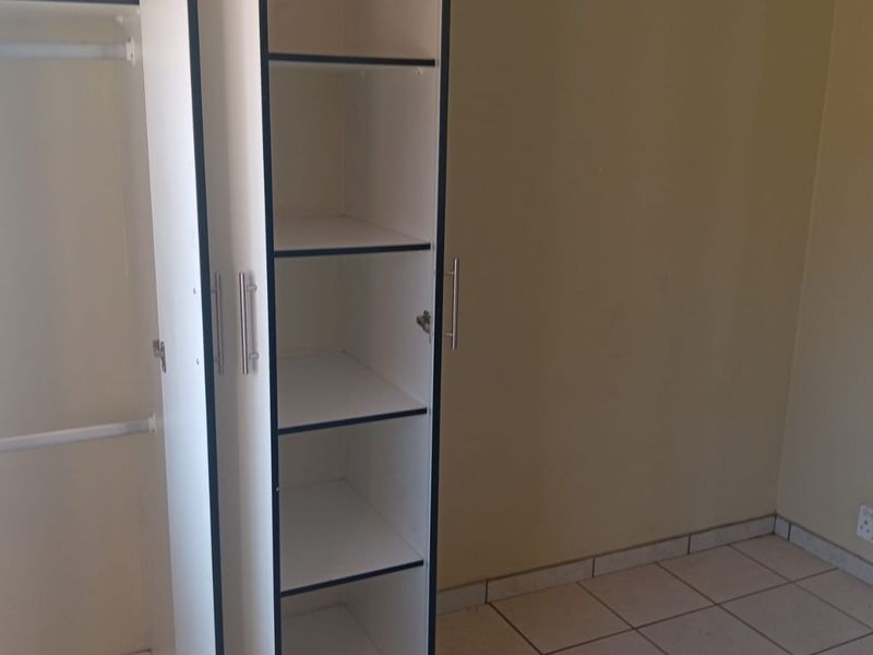 A clean, empty bedroom featuring built-in wardrobe storage and neutral tiled flooring, providing a blank canvas for personalization.