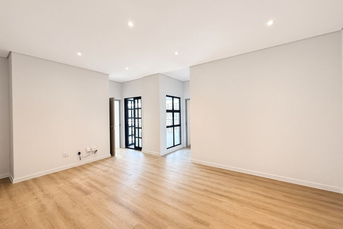 A bright, modern, and empty living area featuring neutral walls, light wood-look laminate flooring, and stylish black-framed glass doors leading to an outdoor space.
