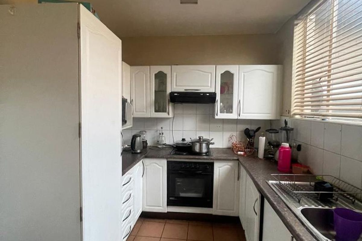 A functional galley-style kitchen featuring white cabinetry, laminate countertops, built-in oven with extractor fan, and tiled flooring.