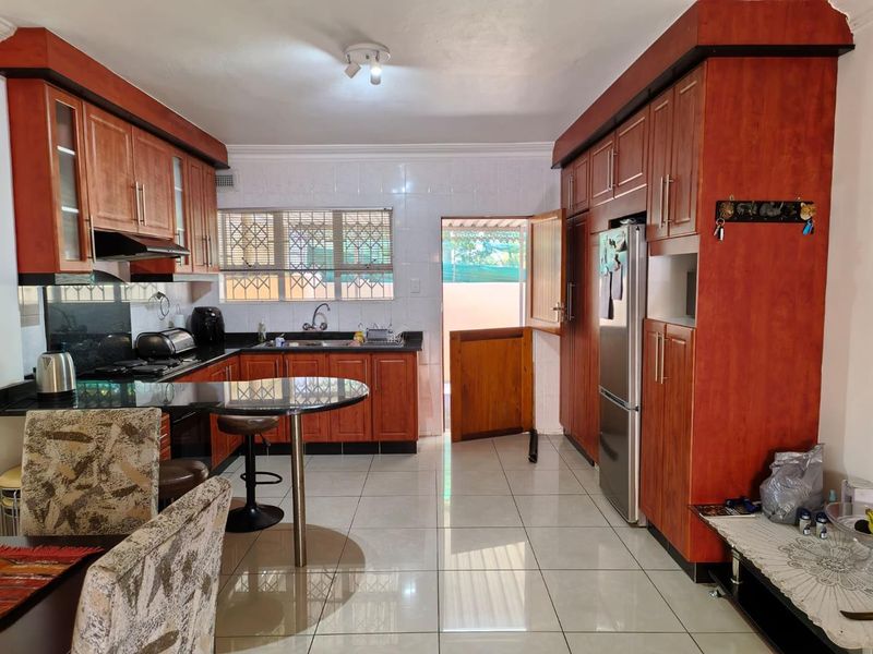 Functional kitchen featuring warm-toned wooden cabinetry, granite countertops, a breakfast bar, and tiled flooring with direct access to the exterior.