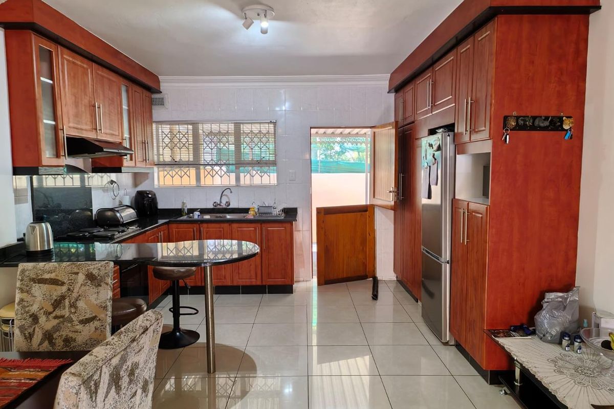 Functional kitchen featuring warm-toned wooden cabinetry, granite countertops, a breakfast bar, and tiled flooring with direct access to the exterior.