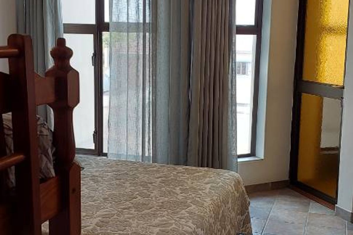 A bedroom featuring tiled flooring, large windows with curtains, and a glass-paneled door leading to an outdoor area.
