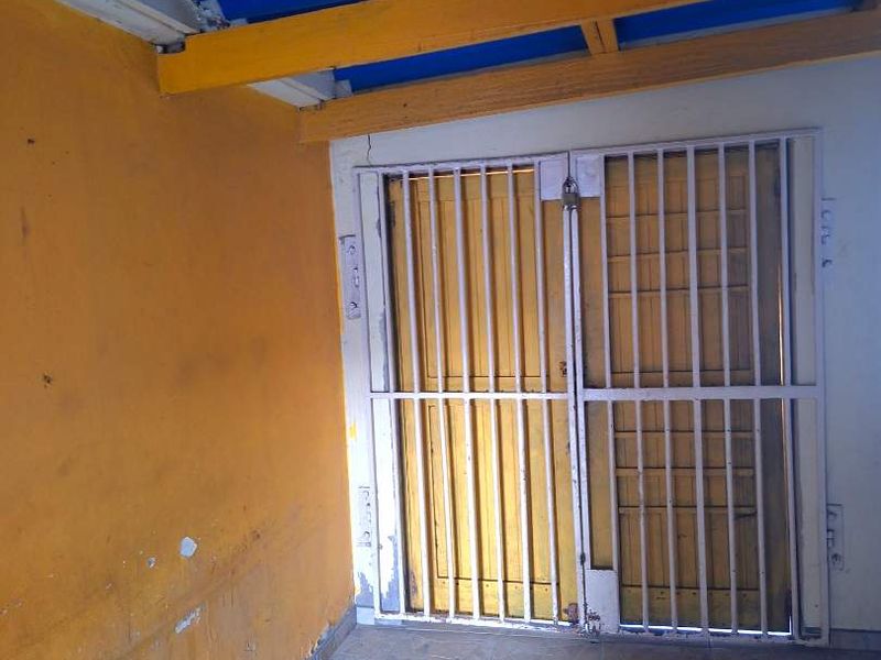 A covered outdoor patio area featuring tiled flooring, exposed timber beams, and a secure metal gate entrance.