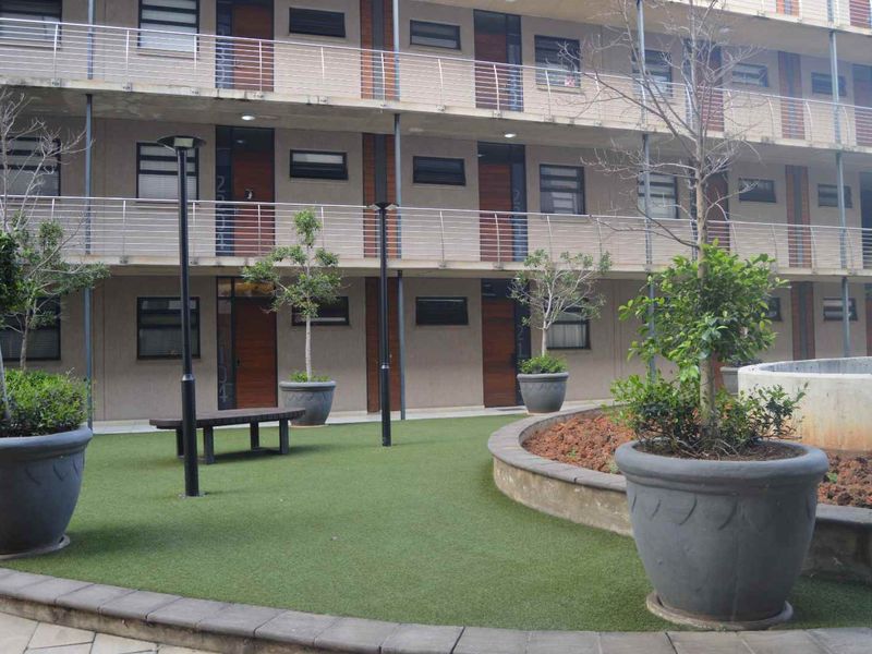A view of the apartment complex courtyard featuring a multi-story facade with balcony railings and a landscaped area with artificial turf.