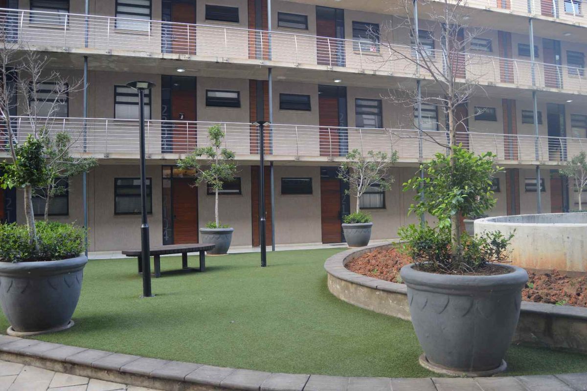 A view of the apartment complex courtyard featuring a multi-story facade with balcony railings and a landscaped area with artificial turf.