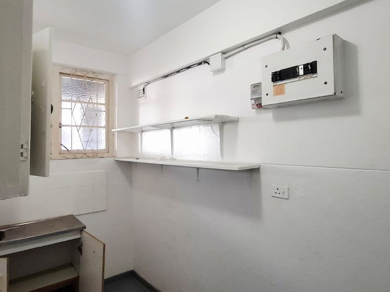 A functional utility or laundry space featuring a stainless steel sink, built-in cabinetry, fixed shelving, and an accessible electrical distribution board.