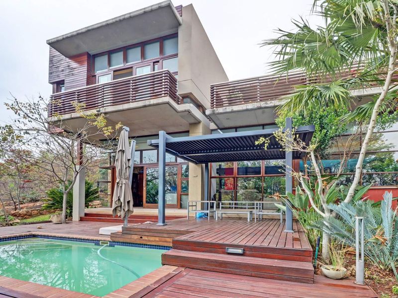 Rear exterior view featuring a modern multi-story residence with timber decking, a louvered pergola, and a swimming pool set in a landscaped garden.
