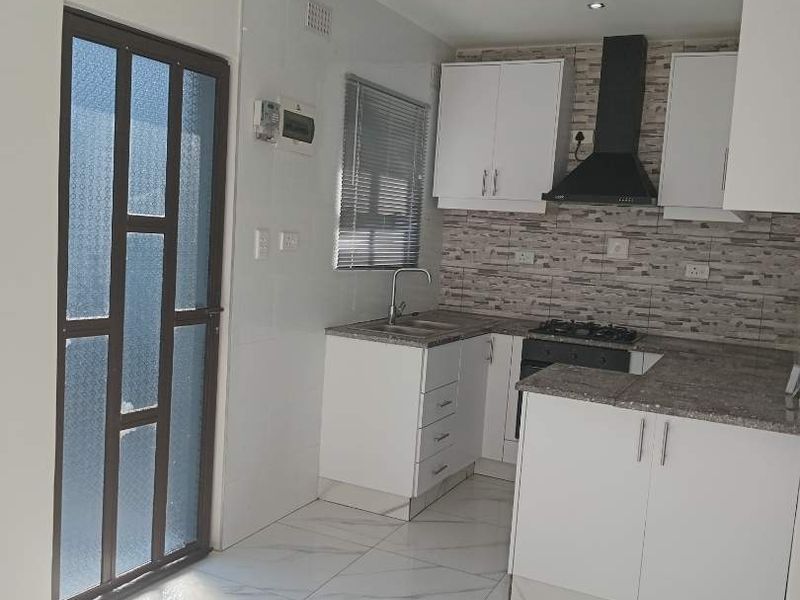 A modern, clean kitchen featuring white cabinetry, granite countertops, a gas hob with extractor fan, and polished marble-look floor tiles.