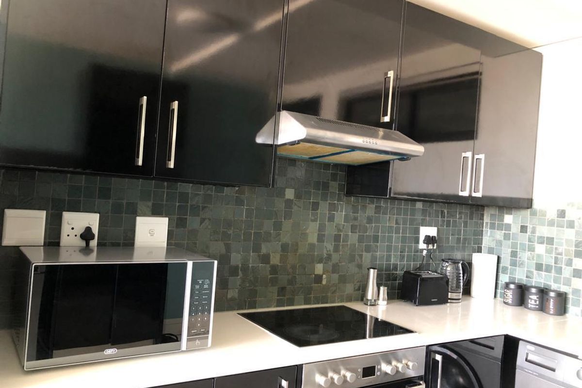 Modern kitchen featuring high-gloss black cabinetry, a stone countertop, a built-in electric hob, an extractor fan, and a tiled backsplash.
