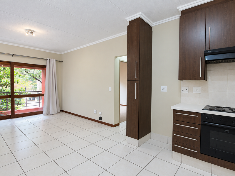 Open-plan living area featuring tiled floors, dark wood kitchen cabinetry with built-in appliances, and a large sliding door leading to an outdoor balcony.