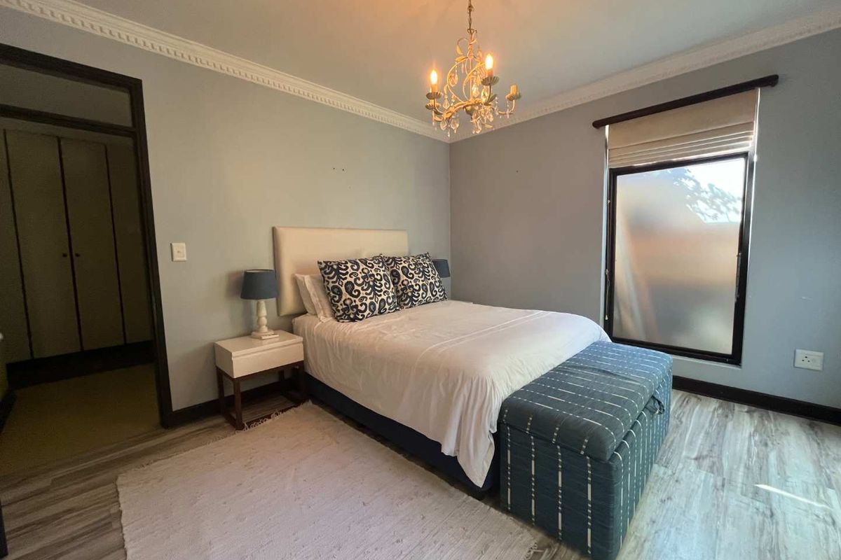 A well-lit bedroom featuring crown molding, wood-look flooring, and a window with a roller blind.