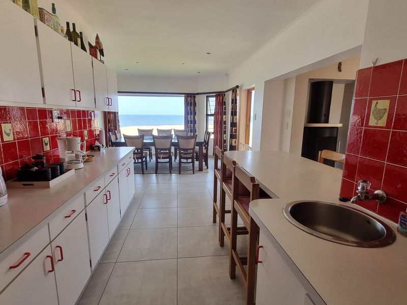 Open-plan kitchen and dining area featuring white cabinetry, red tiled backsplash, breakfast bar, and direct views of the ocean.