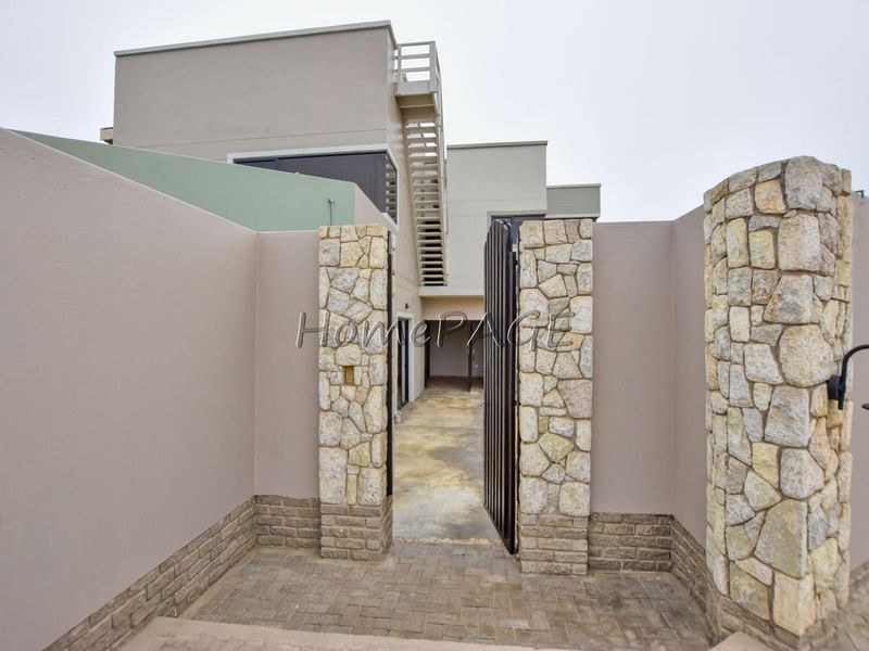 Front entrance featuring stone-clad pillars, a metal gate, and an external staircase leading to the upper level of the modern property.