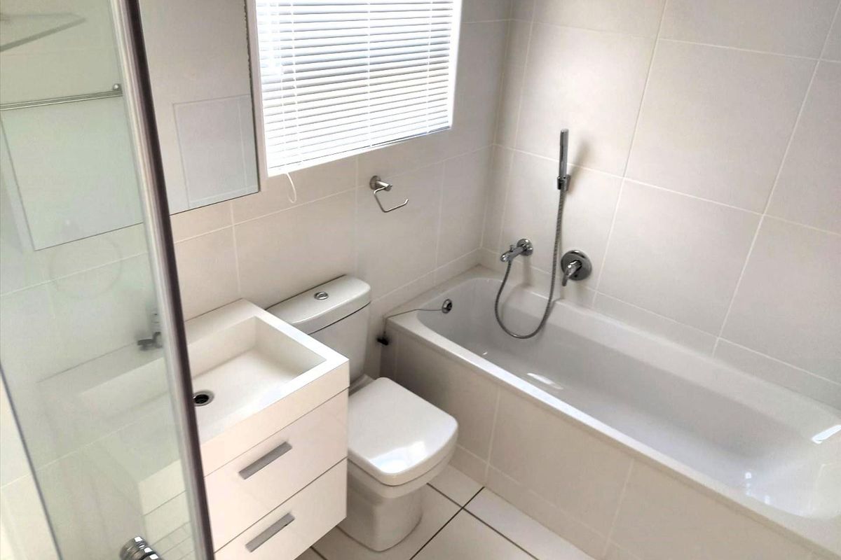 A clean, modern bathroom featuring white wall tiles, a built-in bathtub with handheld shower, a wall-mounted vanity, and a toilet.
