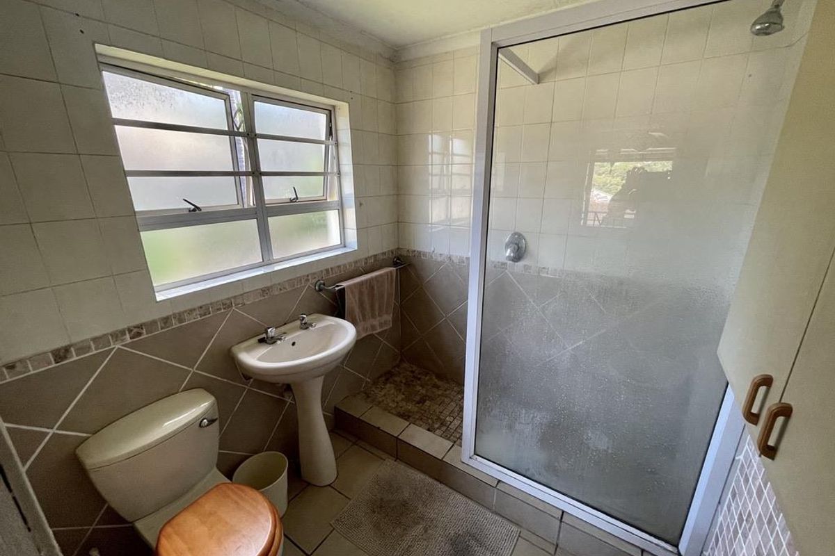 A dated bathroom featuring a pedestal basin, a toilet, and a walk-in shower enclosure with tiled walls and flooring.