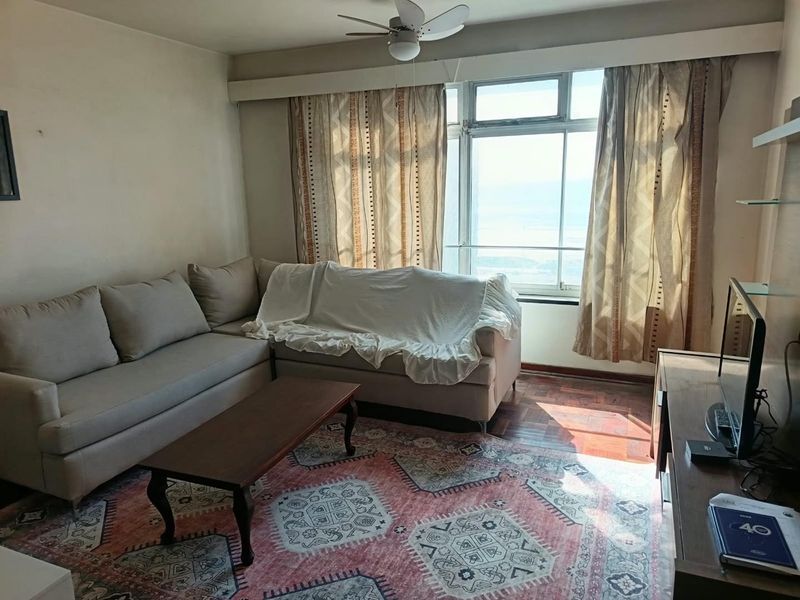 A living room featuring parquet flooring, a ceiling fan, and large windows that provide natural light and exterior views.