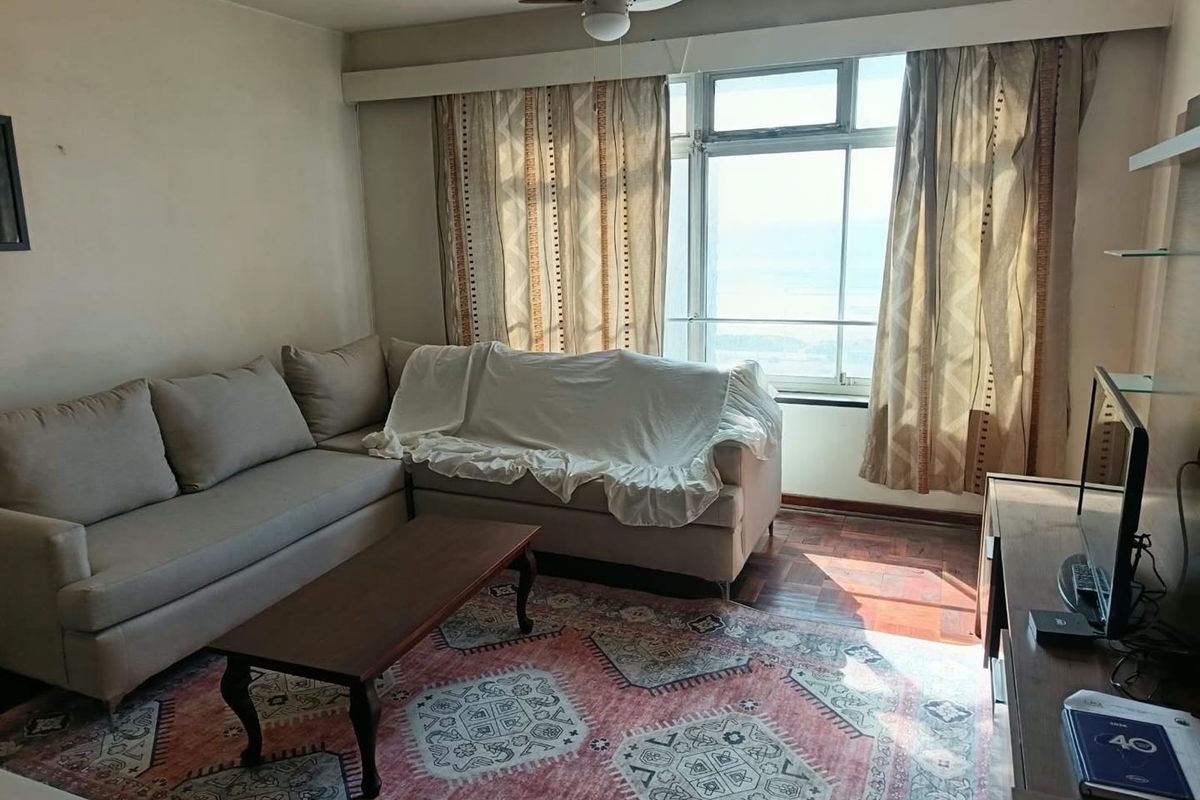 A living room featuring parquet flooring, a ceiling fan, and large windows that provide natural light and exterior views.