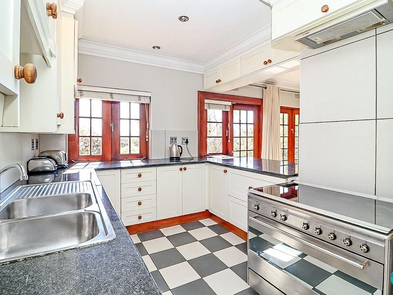 A well-lit kitchen featuring granite countertops, a double stainless steel sink, checkerboard flooring, and classic white cabinetry with wooden accents.