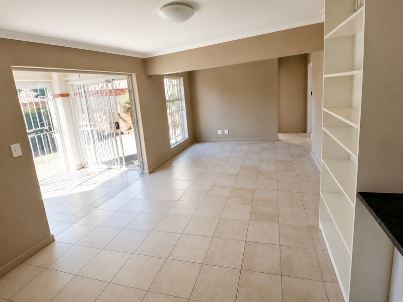 Spacious open-plan living area featuring neutral tiled flooring, built-in shelving, and large sliding glass doors providing direct access to the outdoor space.