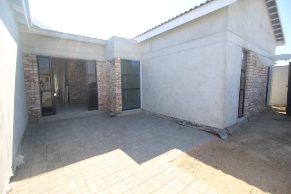 Rear exterior view of a house under construction, featuring a paved patio area, exposed brickwork, and aluminium framed doors and windows.