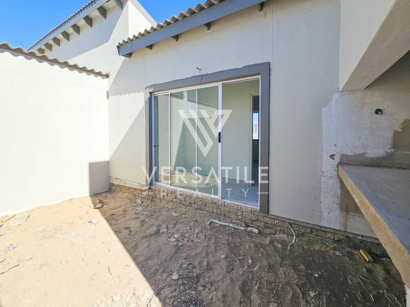 Rear exterior view of a townhouse featuring a sliding glass door and a built-in concrete braai area, currently in an unfinished state.
